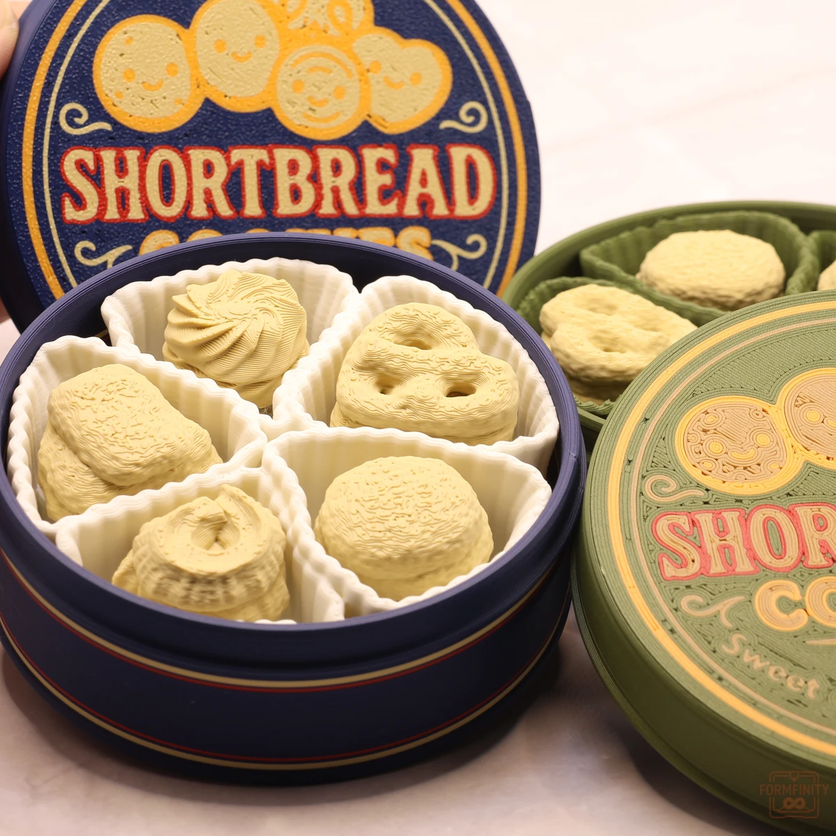 Navy and green 3D printed shortbread cookie tins with the lids off, cookies in paper cups